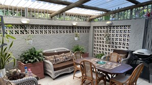 An outdoor patio area with wicker furniture, a dining table, and a grill. - Eden Rose Manor (La Mercy)