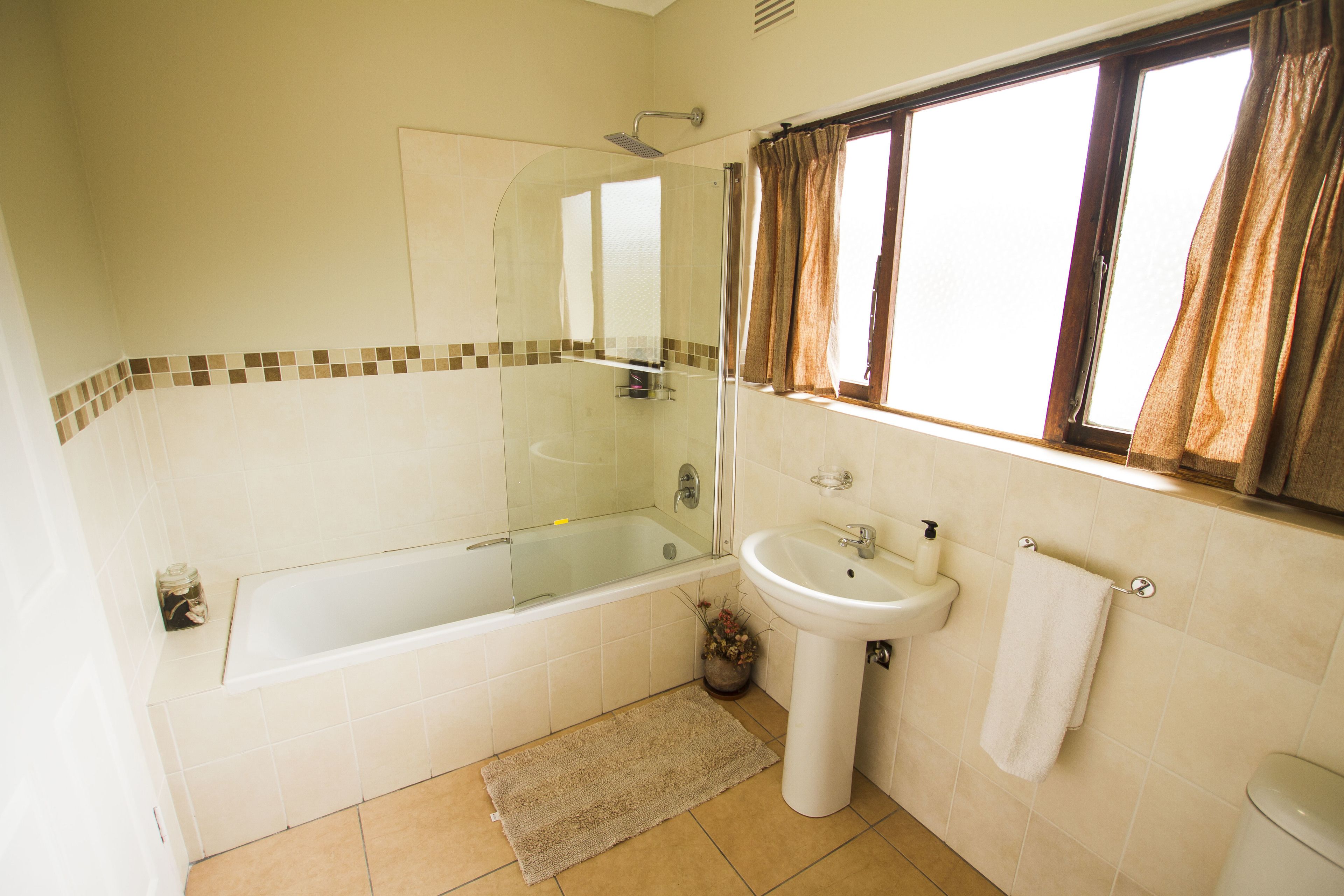Une salle de bain avec une douche à parois de verre, un lavabo blanc et une fenêtre avec des rideaux.
