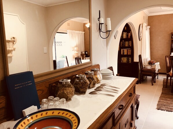 A hotel room with a large mirror, a wooden dresser, and a dining area with a table and chairs.