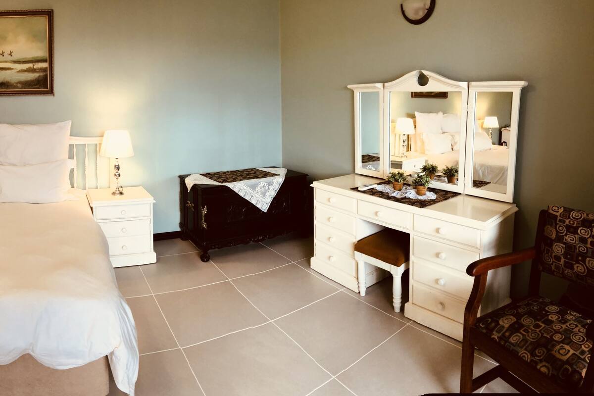 A neatly arranged bedroom with a large bed, bedside tables, a dresser, and a mirror.