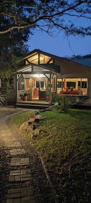 Una casa moderna con un porche de cristal, un camino de entrada pavimentado y un césped cuidado.