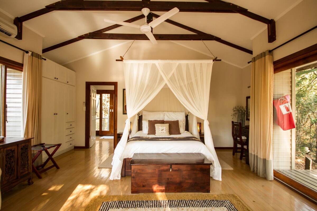 A bedroom with a canopy bed, wooden floor, and a ceiling fan.