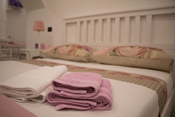 A neatly made bed with pink and white towels, a floral-patterned bedspread, and a white headboard.