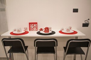A dining table with red and white tableware, black chairs, and a wall-mounted light switch.