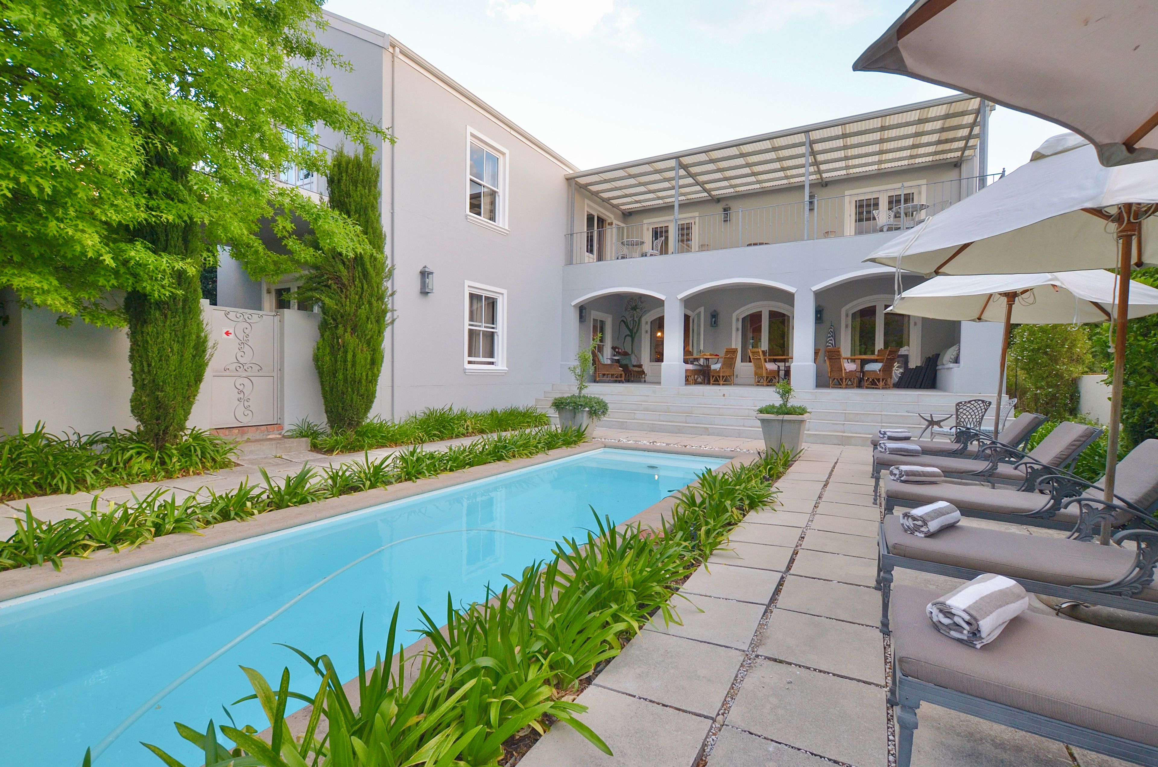 A pool area with lounge chairs, a covered seating area, and a building with multiple windows and balconies.
