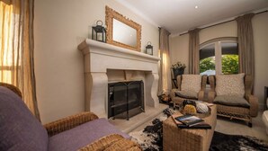 Un salon chaleureux avec une cheminée, des meubles en osier et une vue sur la verdure environnante.