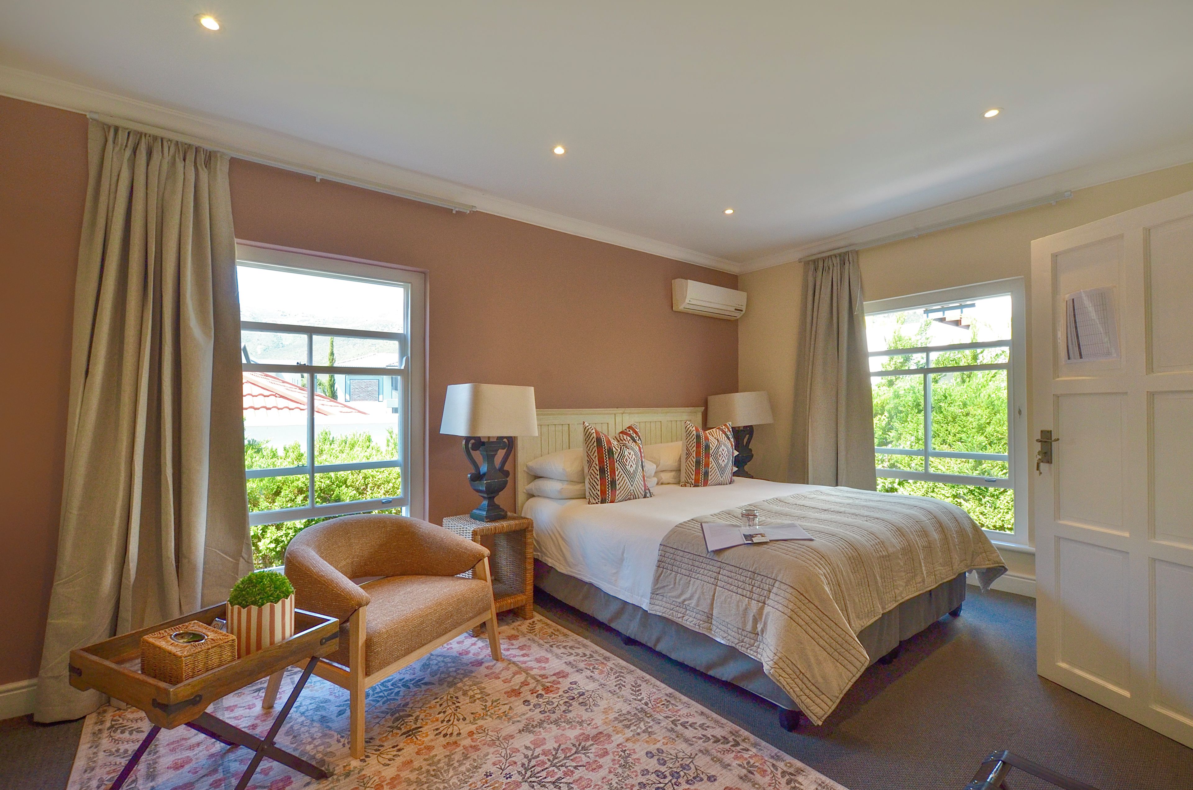 A hotel room with a bed, a chair, a small table with a plant, and a window with curtains.