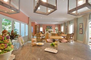 Un vaste espace dédié à la salle à manger, avec une grande table en granit, des chaises en osier et une vue sur l’extérieur grâce à de grandes fenêtres.