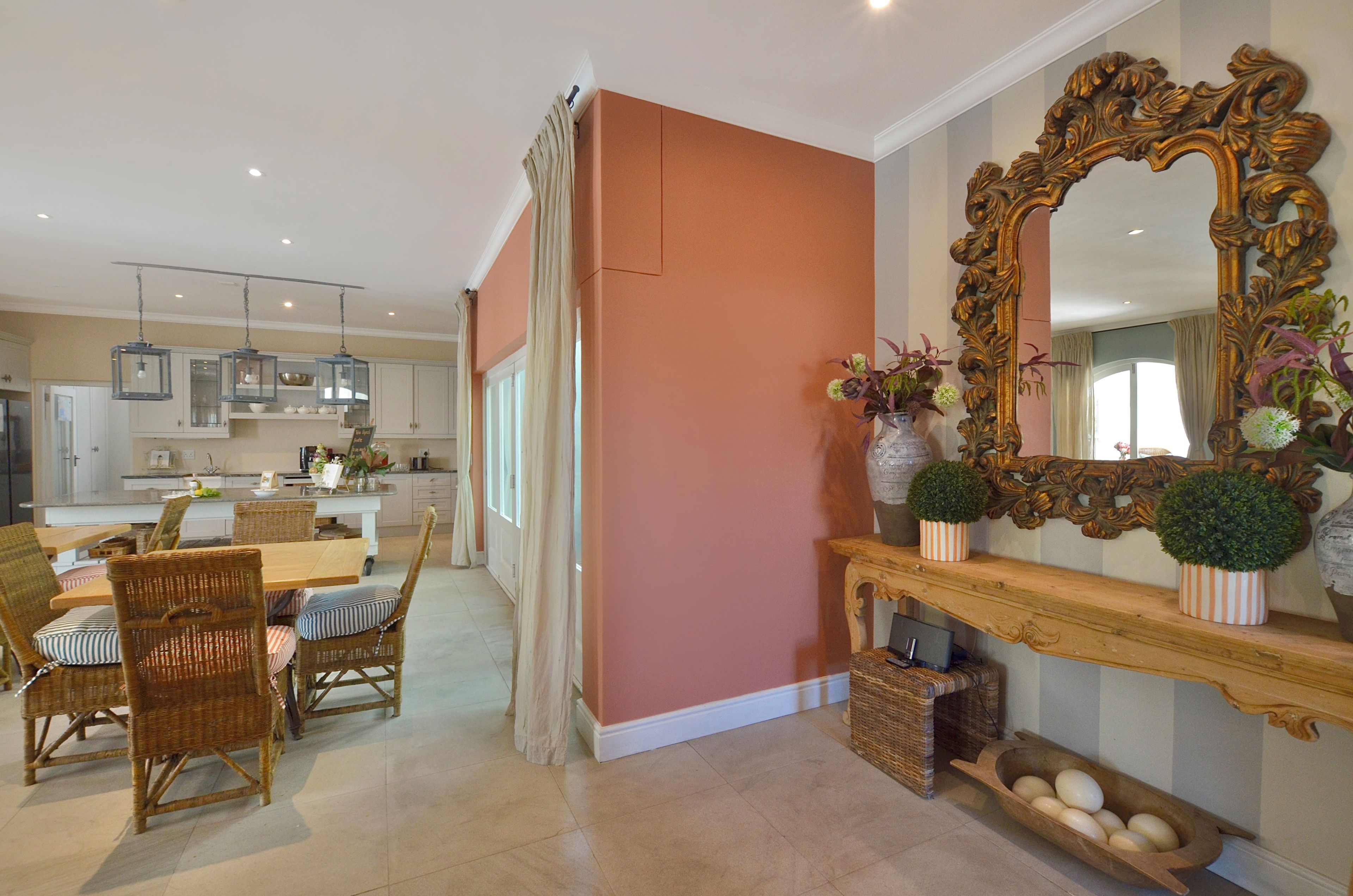 Una cocina amplia con electrodomésticos modernos, un comedor con mobiliario de mimbre y un espejo grande y decorativo sobre un aparador.