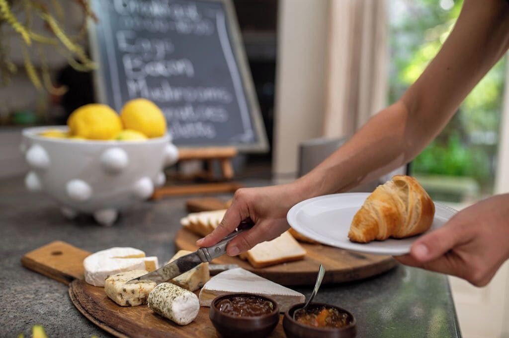 A person serving a croissant and cheese on a plate.
