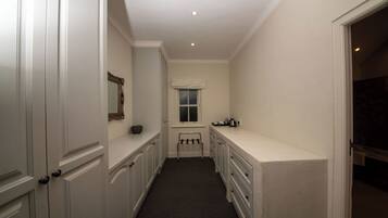 A narrow hallway with white walls and a window. There is a small bench and a coat rack near the window.