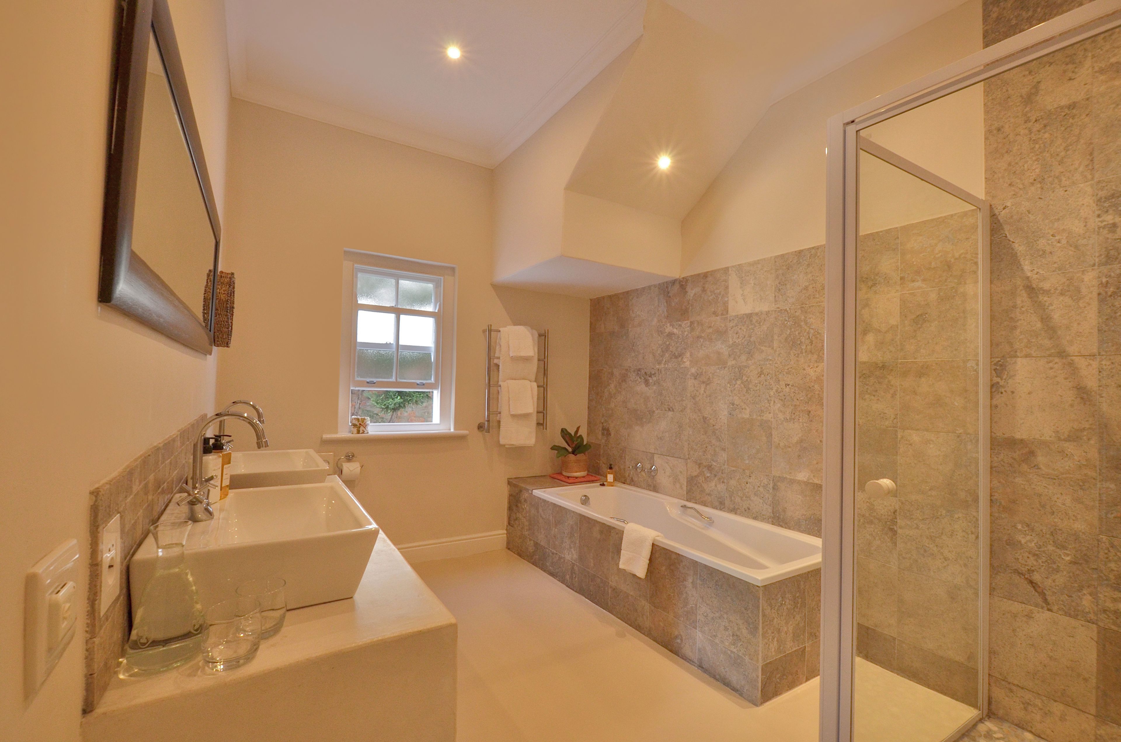 A modern bathroom with a double sink, a bathtub, and a glass-enclosed shower.