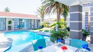 An outdoor pool area with a dining setup, including chairs and a table with a vase of flowers. - Atlantic Beach Villa (Cape Town)