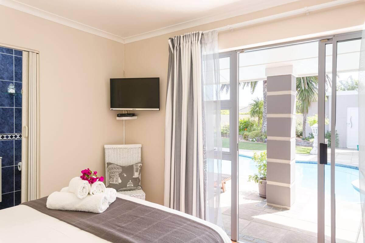 Quarto de hotel com cama, televisão, banheiro e vista para uma piscina.