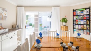 A dining area with a wooden table set for four, white chairs, and a buffet station with a toaster and bread basket. - Atlantic Beach Villa (Cape Town)