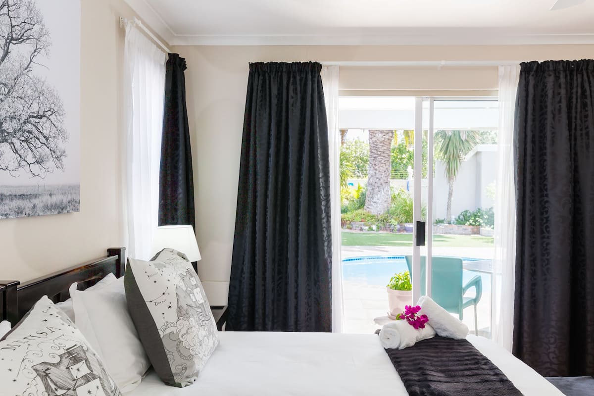 Quarto de hotel com uma cama, vista da piscina e varanda com cadeira e planta em vaso.