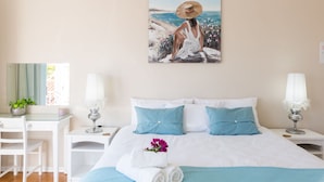 A bedroom with a bed, two nightstands, a desk, and a chair. There is a painting on the wall and a window with curtains. - Atlantic Beach Villa (Cape Town)