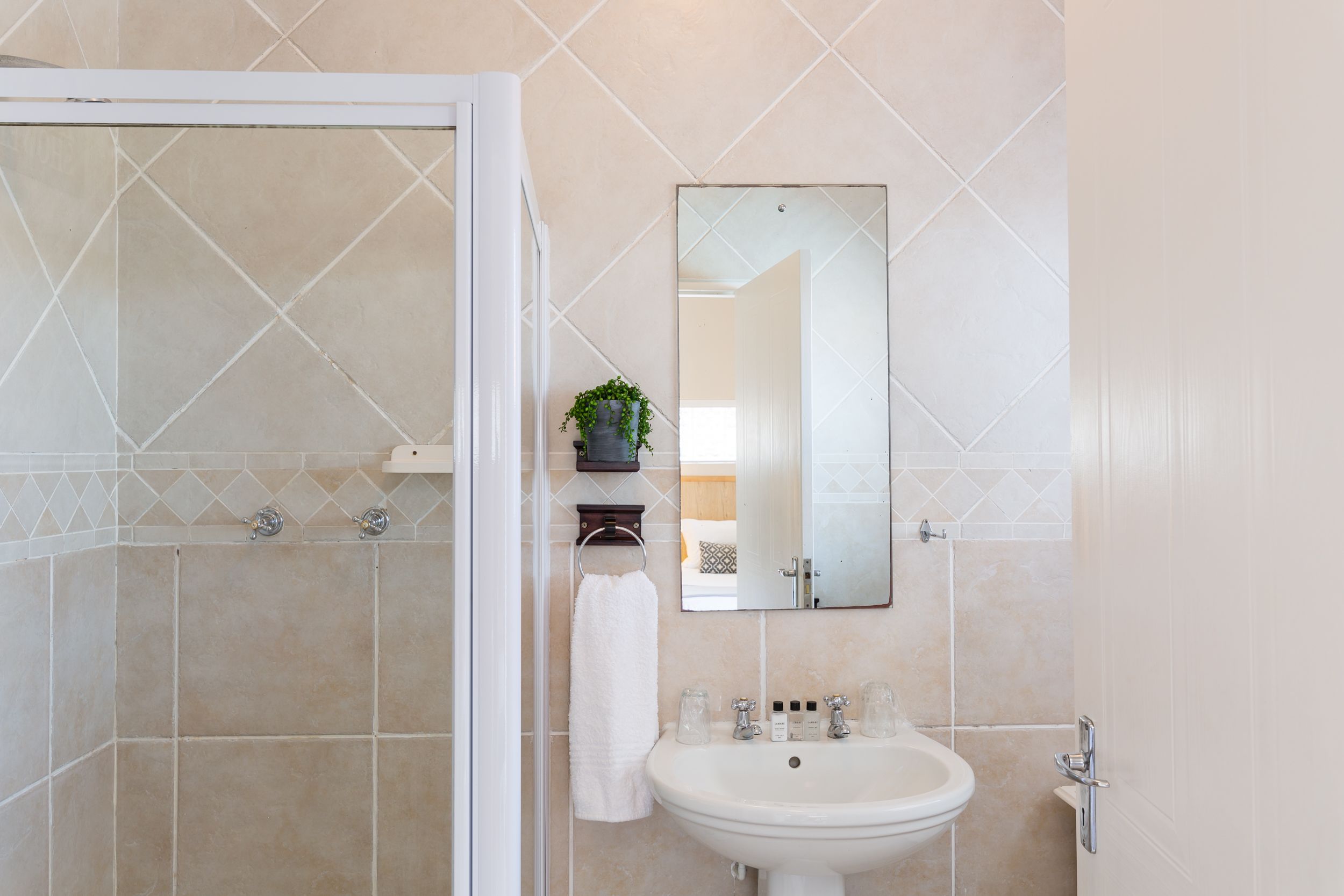 A bathroom with a shower, a sink, a mirror, and a towel rack.