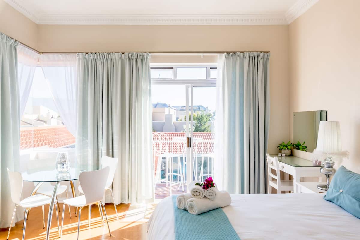 Quarto de hotel com cama, escrivaninha, cadeira e vista para a varanda.