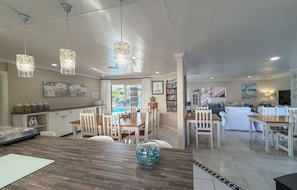 A spacious kitchen with white cabinetry, a dining area with a wooden table and chairs, and a living room with a sofa and a TV. - Atlantic Beach Villa (Cape Town)