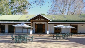 A building with a green roof and a covered patio area with green metal chairs and umbrellas. - Waterwoods Cottages (Fort Nottingham)