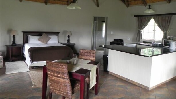 A room with a bed, a dining table with chairs, a kitchen area, and a large window. - Waterwoods Cottages (Fort Nottingham)