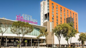 A modern hotel with a prominent 'VIA' sign, a glass facade, and a mix of orange and white buildings.