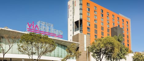 Un hotel moderno con un cartello 'VIA' ben visibile, una facciata in vetro e un mix di edifici arancioni e bianchi.