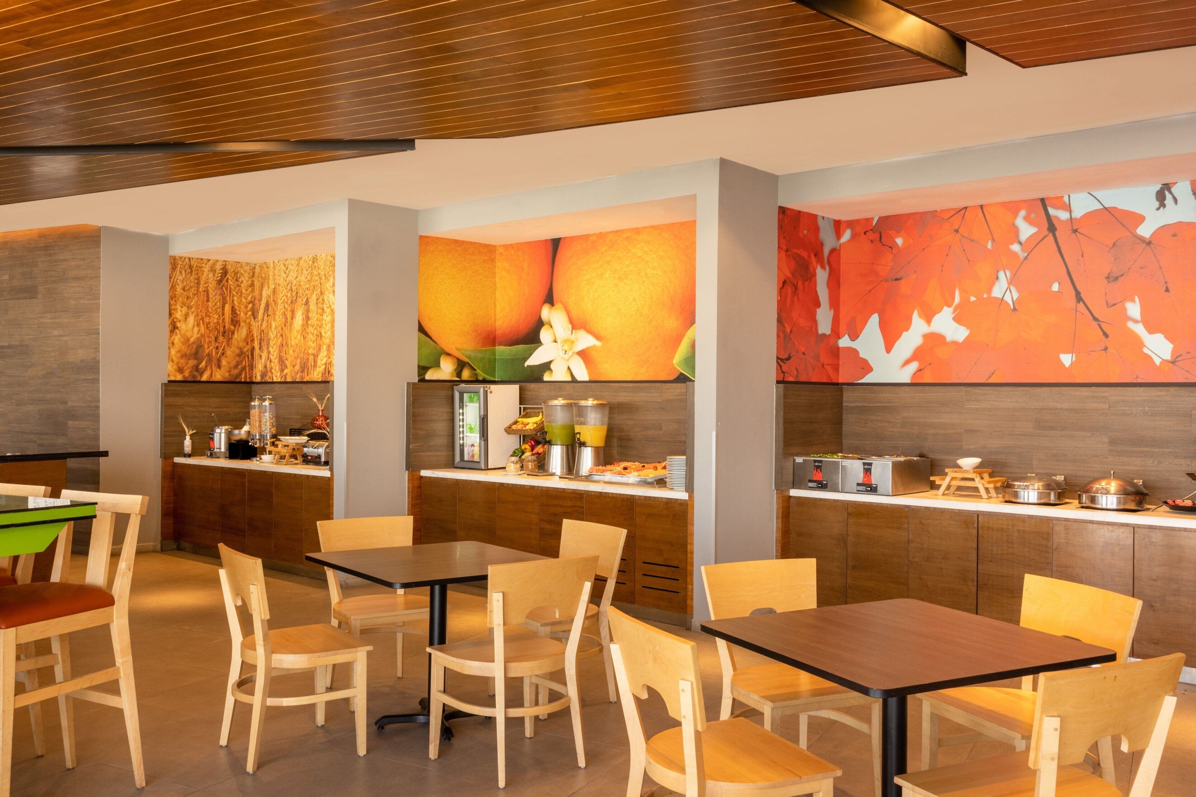 Un restaurante moderno con mobiliario de madera, una barra con productos alimenticios y una pared decorada con motivos de frutas y hojas.