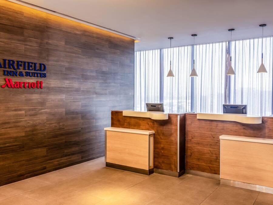 Un mostrador de recepción con un panel de pared de madera, un logotipo de Marriott y una ventana con persianas verticales.