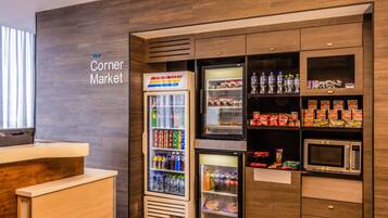 A corner market with a refrigerator, microwave, and shelves stocked with snacks and beverages.