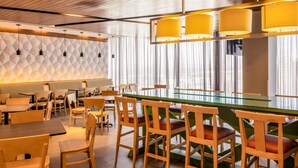 A modern restaurant with a geometric patterned wall, wooden ceiling, and a bar area with stools.