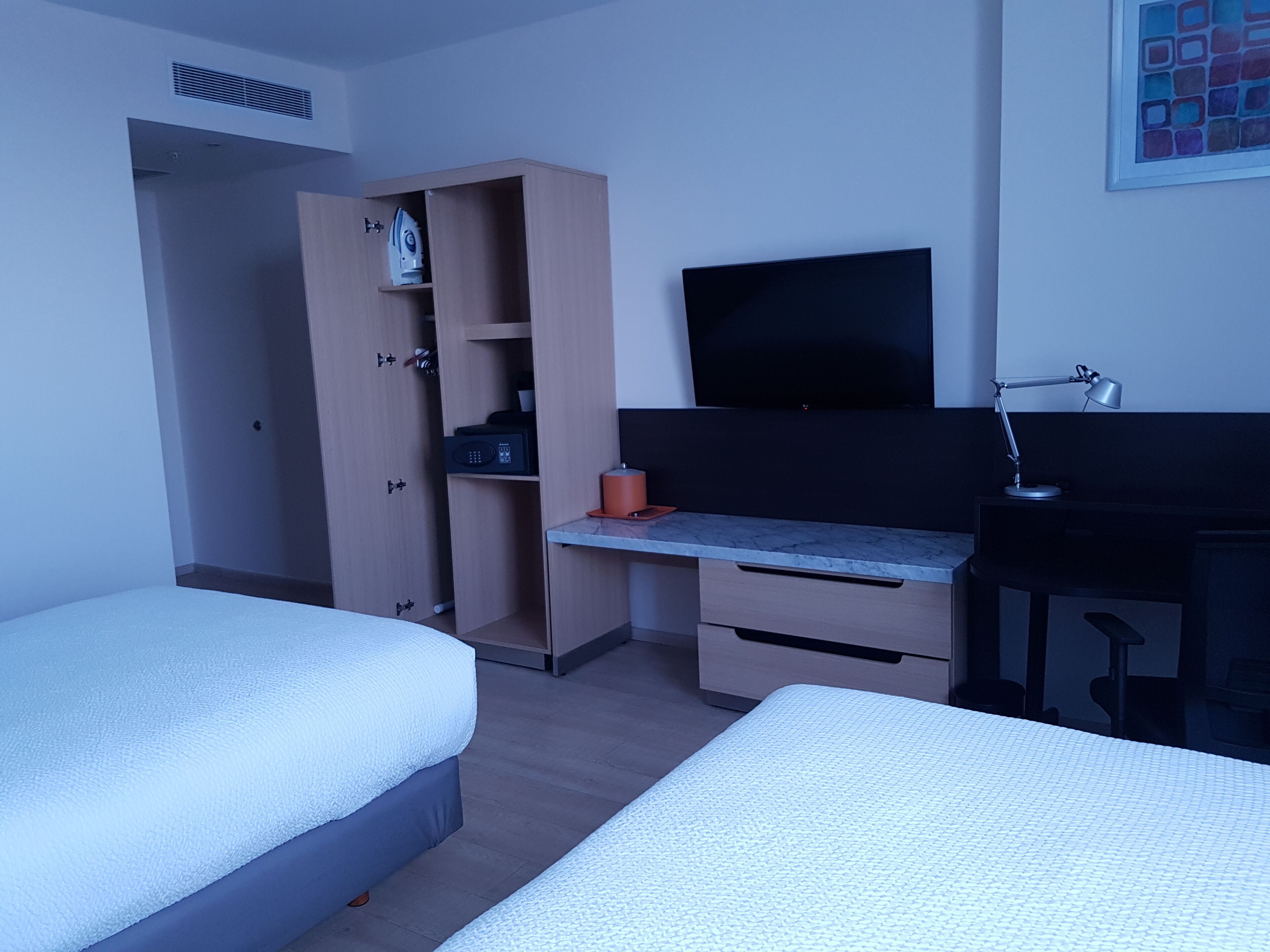 Una habitación de hotel con dos camas, un escritorio con computadora, televisión y armario.