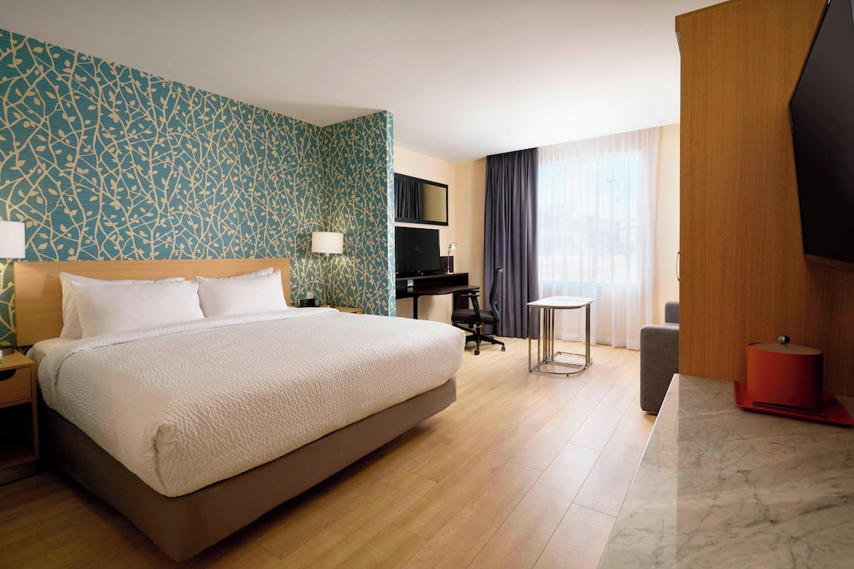 Ein Hotelzimmer mit einem großen Bett, einem Schreibtisch, einem Stuhl, einem Fernseher und einem Fenster mit Vorhängen.
