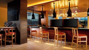 A modern bar area with wooden chairs, a flat-screen TV, and pendant lighting.