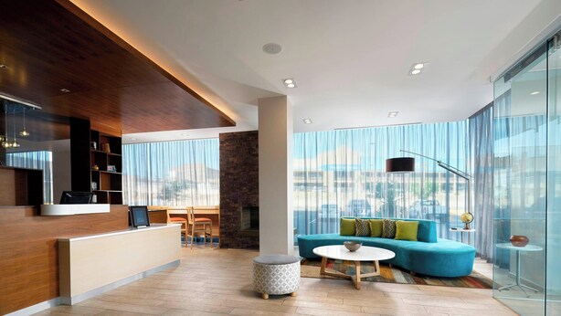 A modern hotel lobby with a reception desk, seating area, and large windows offering a city view.