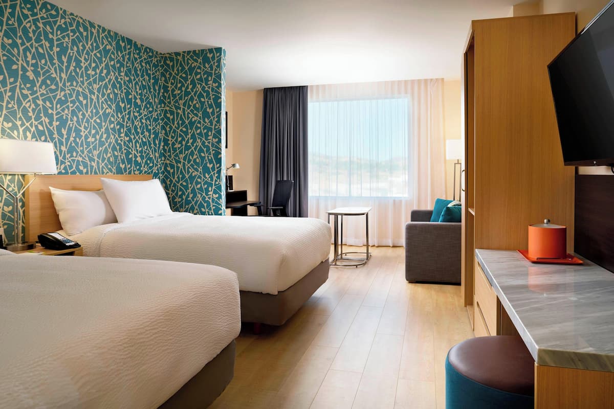 Ein Hotelzimmer mit zwei Betten, einem Schreibtisch, einem Fernseher und Blick ins Freie.