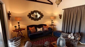 Un salon chaleureux avec un canapé bleu foncé, des fauteuils à motifs et une table basse en bois. Un miroir décoratif orne le mur, et une petite table d’appoint avec une lampe se trouve à proximité.