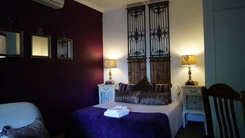 A bedroom with a bed, two bedside tables with lamps, a chair, and a wall with three framed pictures.