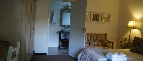Hotelkamer met een bed, nachtkastje met lamp, stoel, kledingkast en een zichtbare badkamer door een geopende deur.