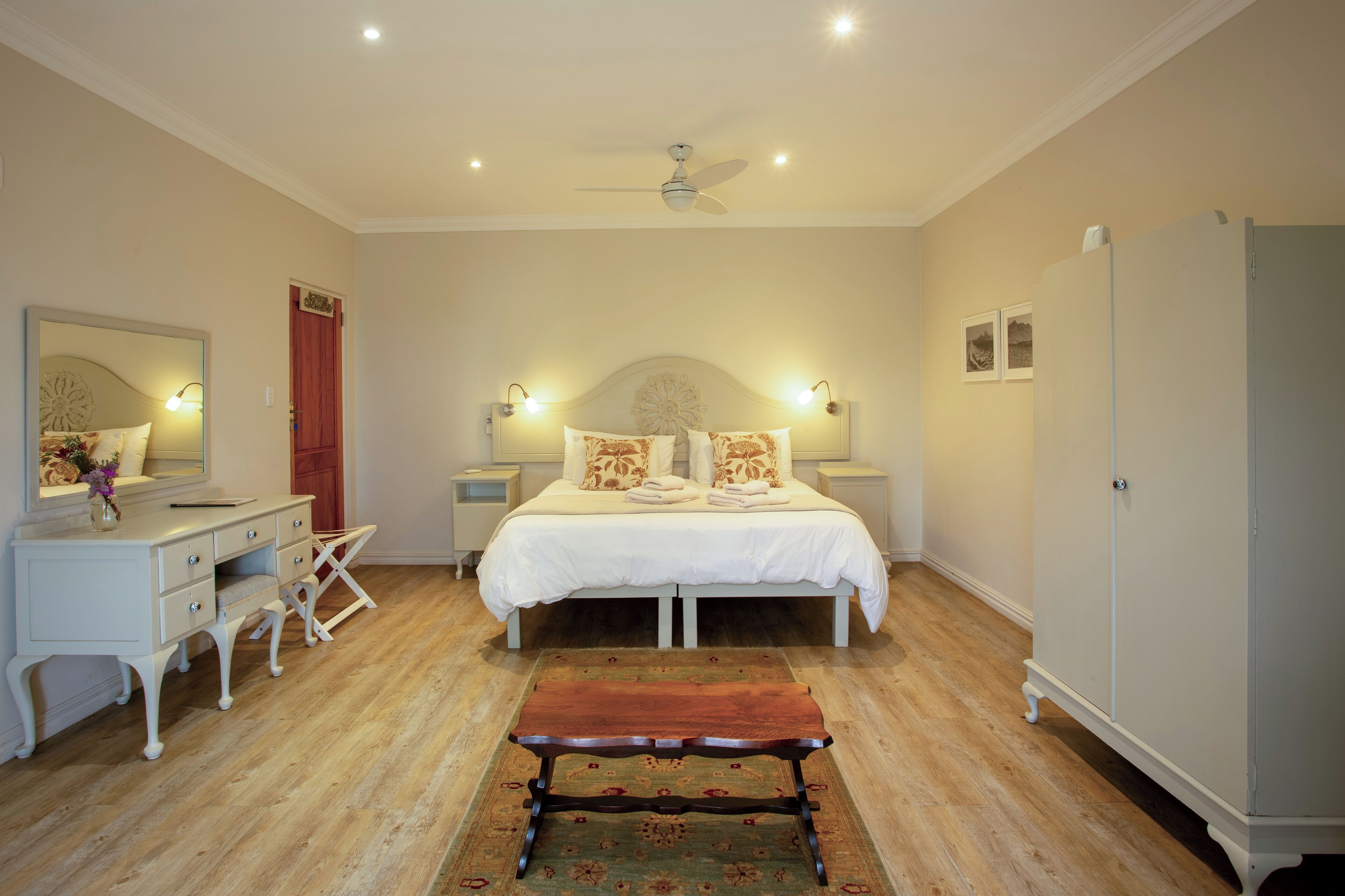 Een slaapkamer met een bed, nachtkastjes, een spiegel, een kledingkast en een plafondventilator.