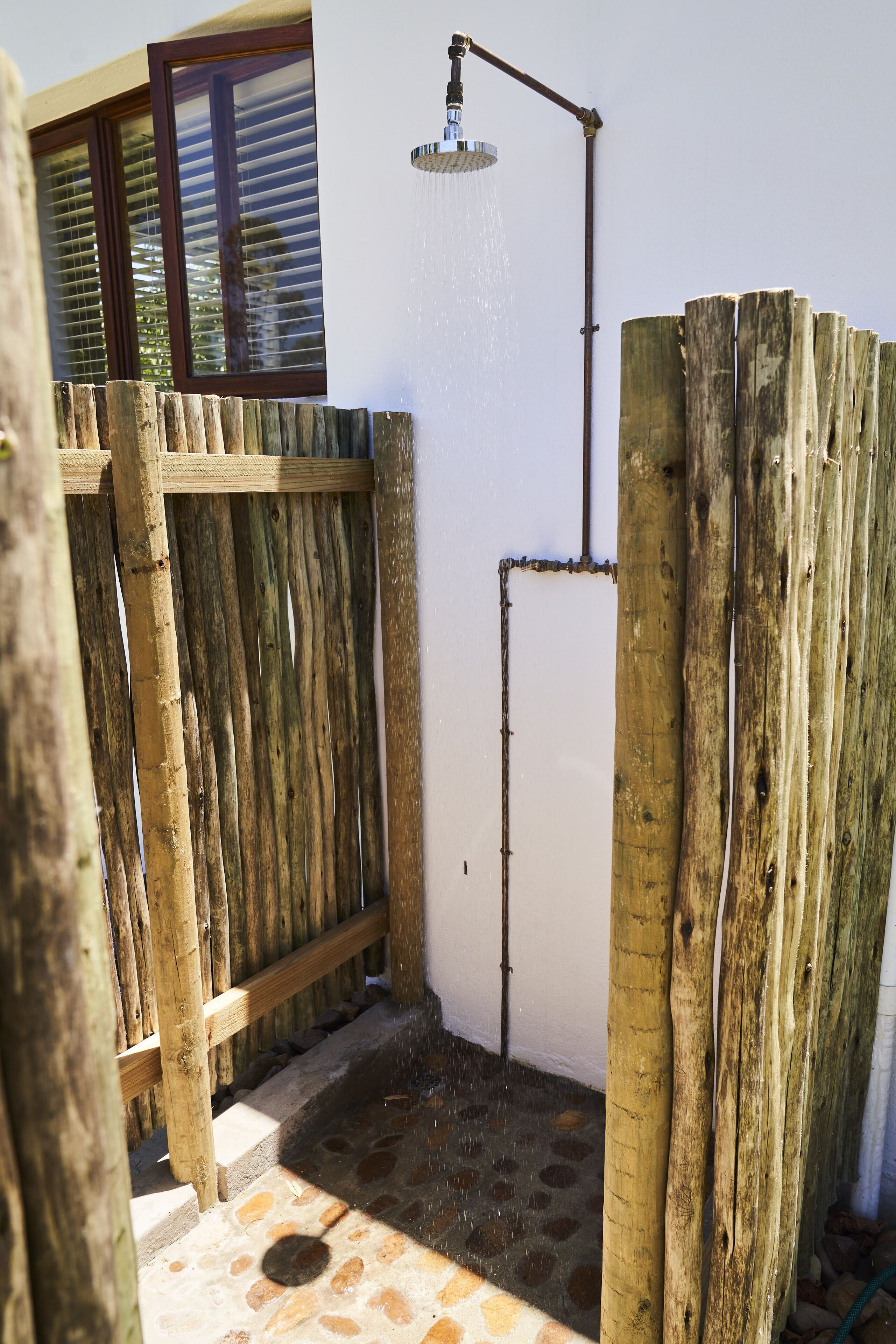 A wooden fence surrounding a shower area with a metal pipe and a window above.
