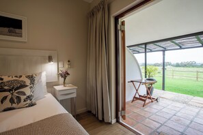 A bedroom with a bed, bedside table, and a view of a garden through a sliding door.