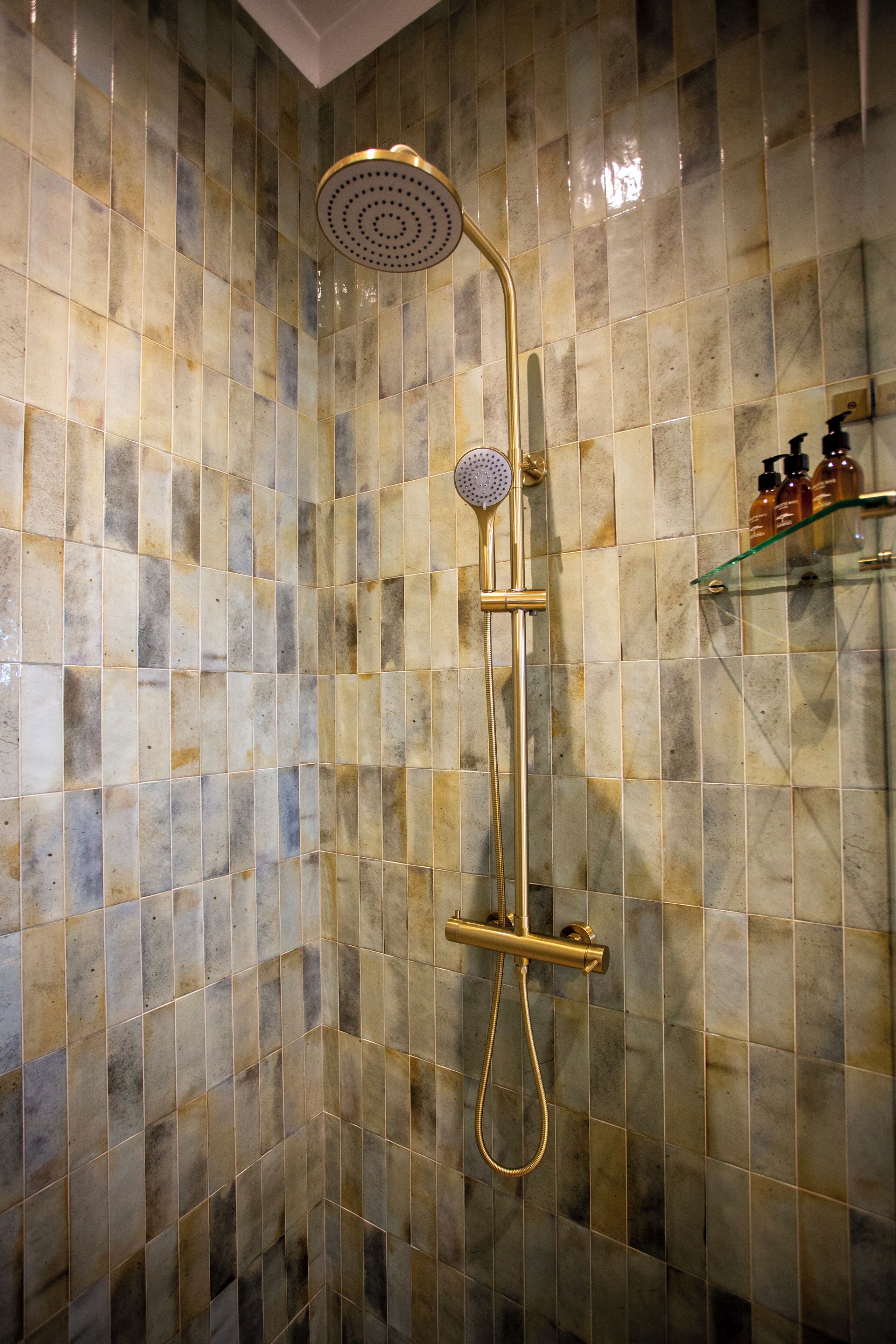 A shower with a gold fixture and a tiled wall.