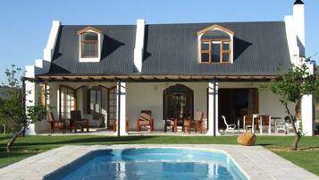 A two-story house with a covered patio, a swimming pool, and outdoor furniture.