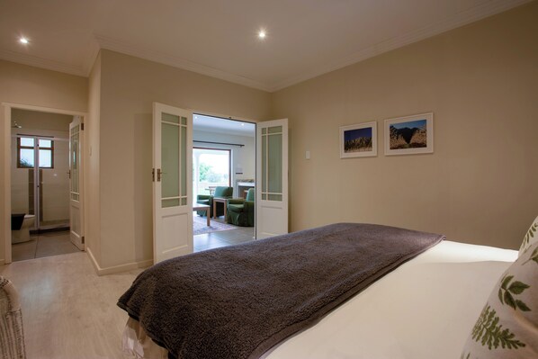 A bedroom with a large bed, a door leading to a bathroom, and a view of a dining area.