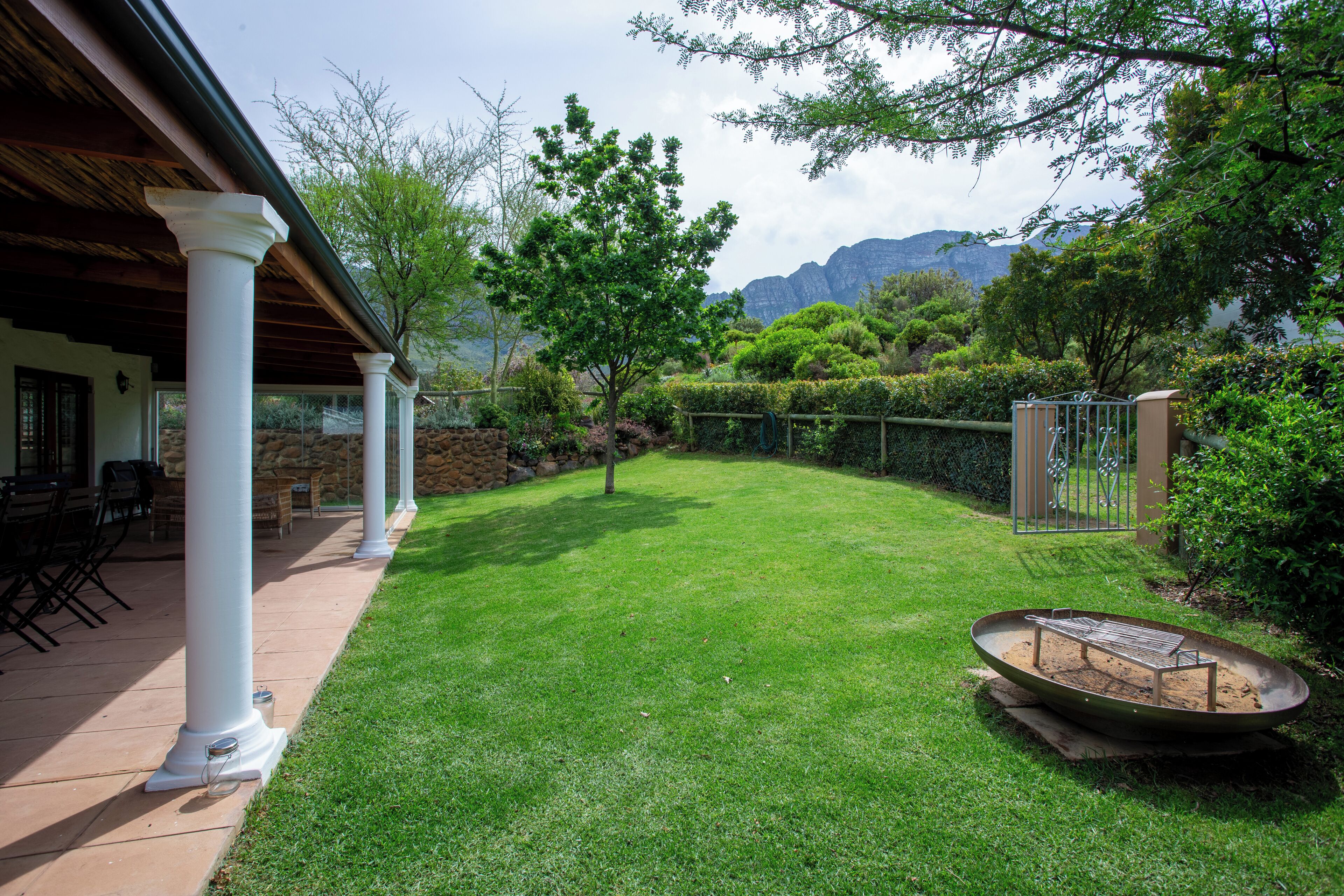 A well-maintained lawn with a fire pit, white columns, and a stone wall.