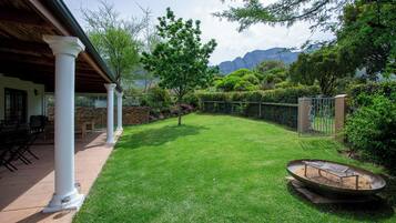 A well-maintained lawn with a fire pit, white columns, and a stone wall.