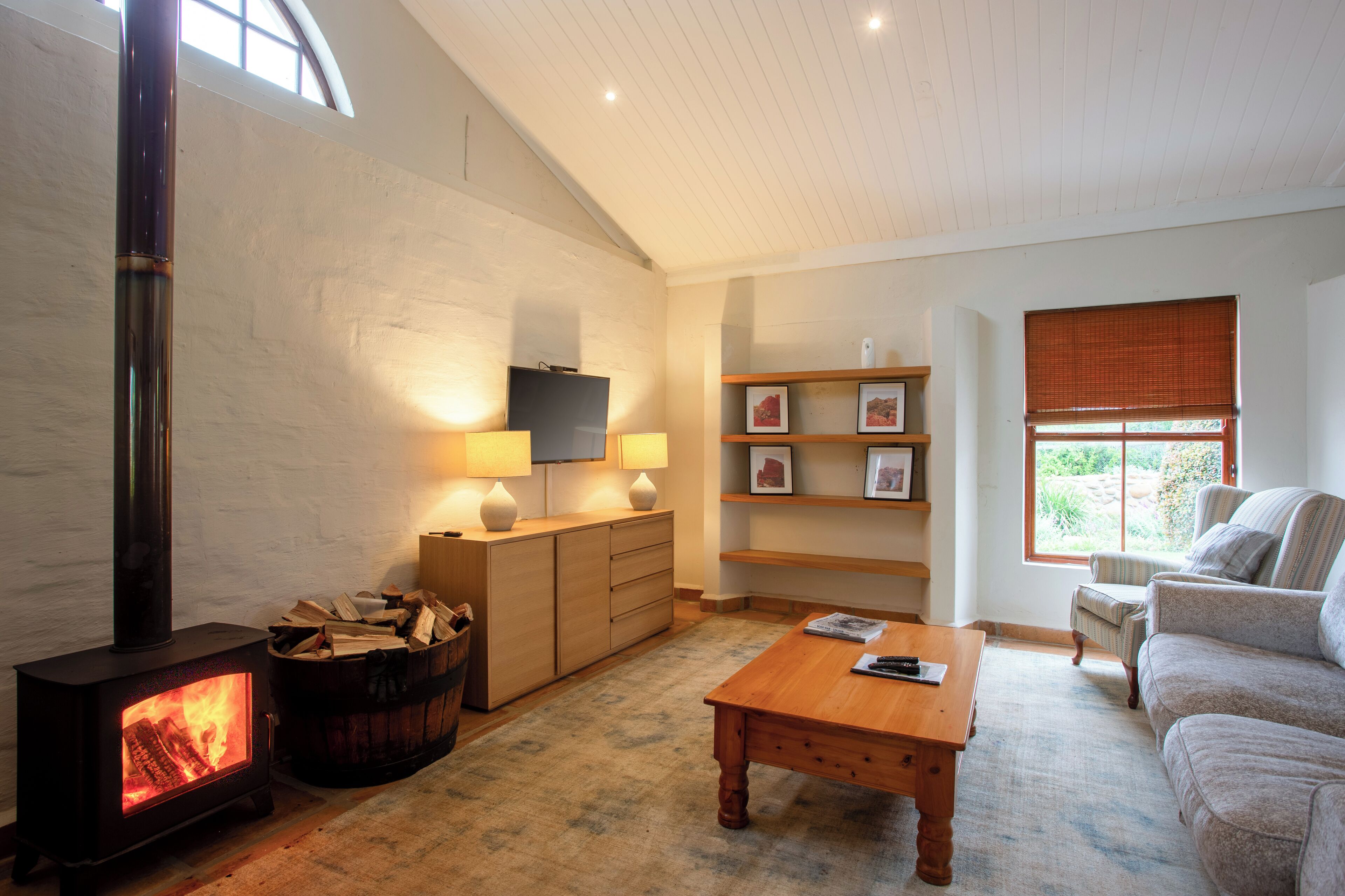 A cozy living room with a wood-burning stove, a television on a stand, a sofa, a coffee table, and a bookshelf.