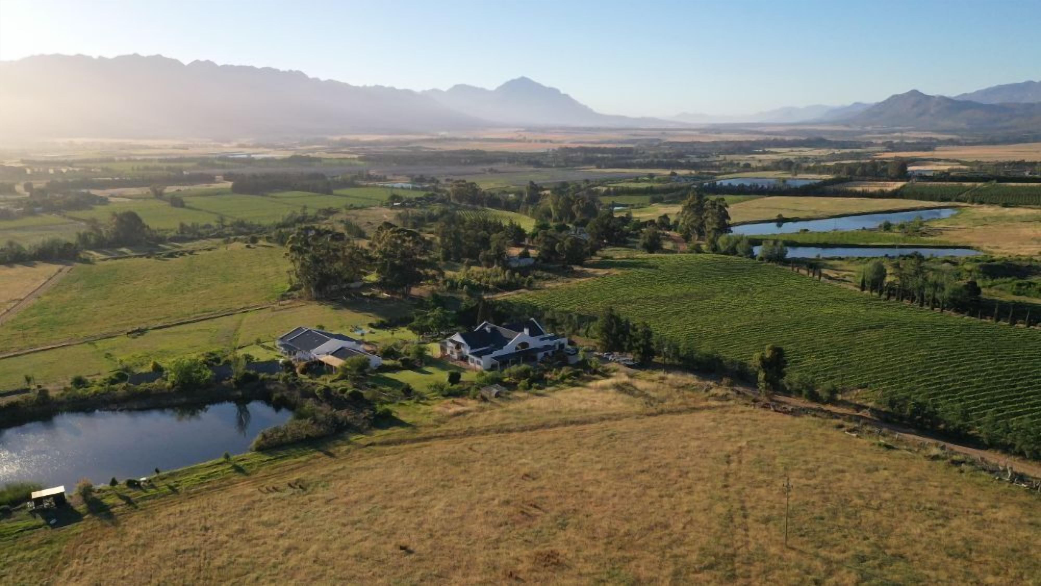 A rural landscape with a large house surrounded by fields and a lake.